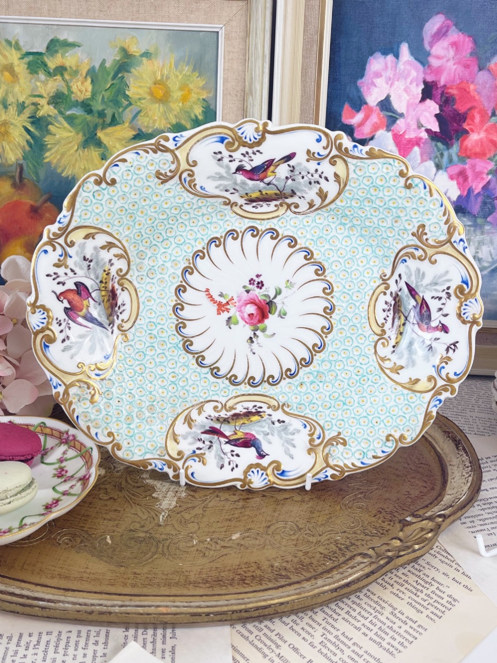 An oval antique porcelain serving dish featuring hand-painted birds in cartouches, a central pink rose, a turquoise pattern ground, and a scalloped gilded rim.