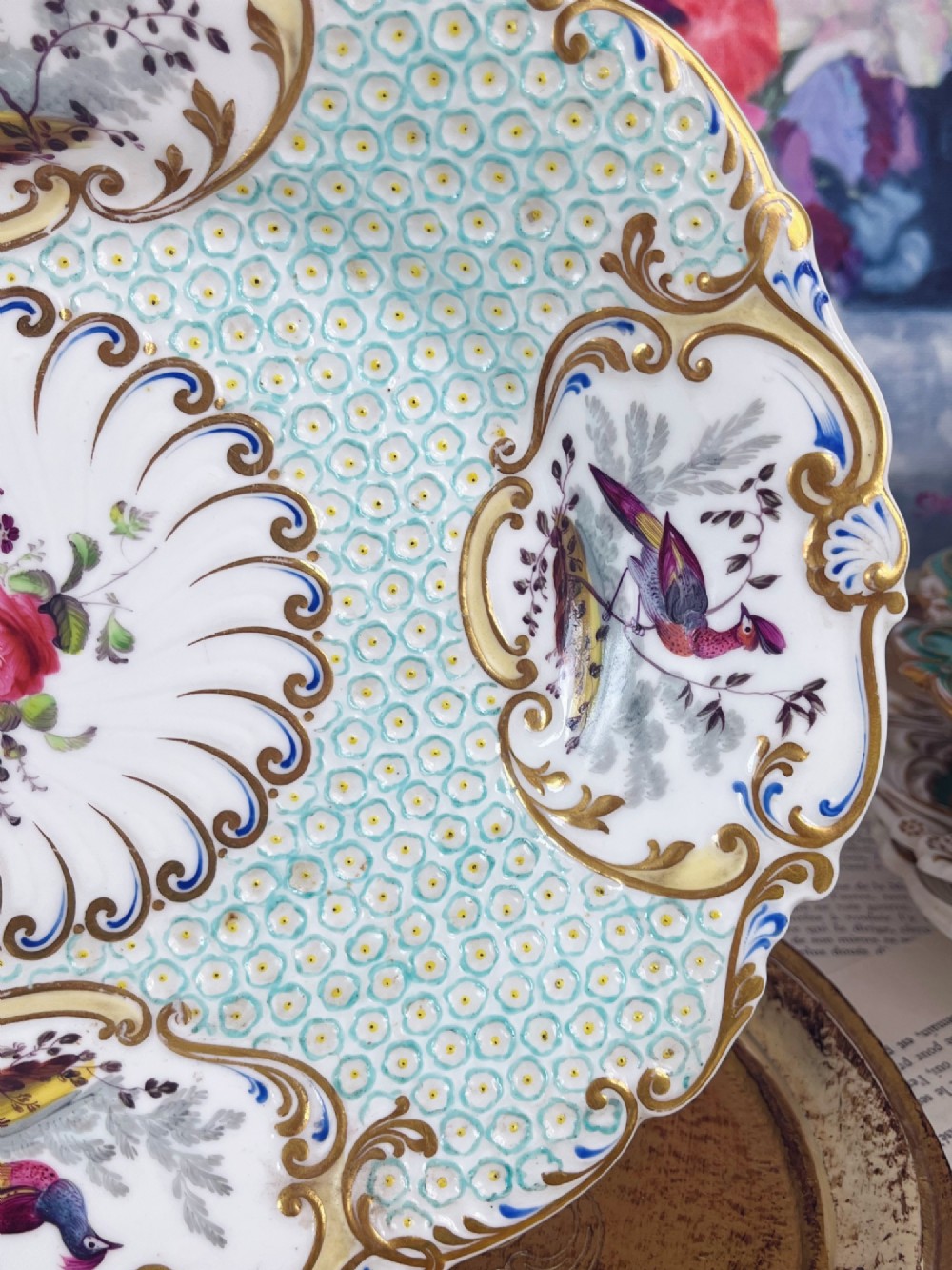 An oval antique porcelain serving dish featuring hand-painted birds in cartouches, a central pink rose, a turquoise pattern ground, and a scalloped gilded rim. View III