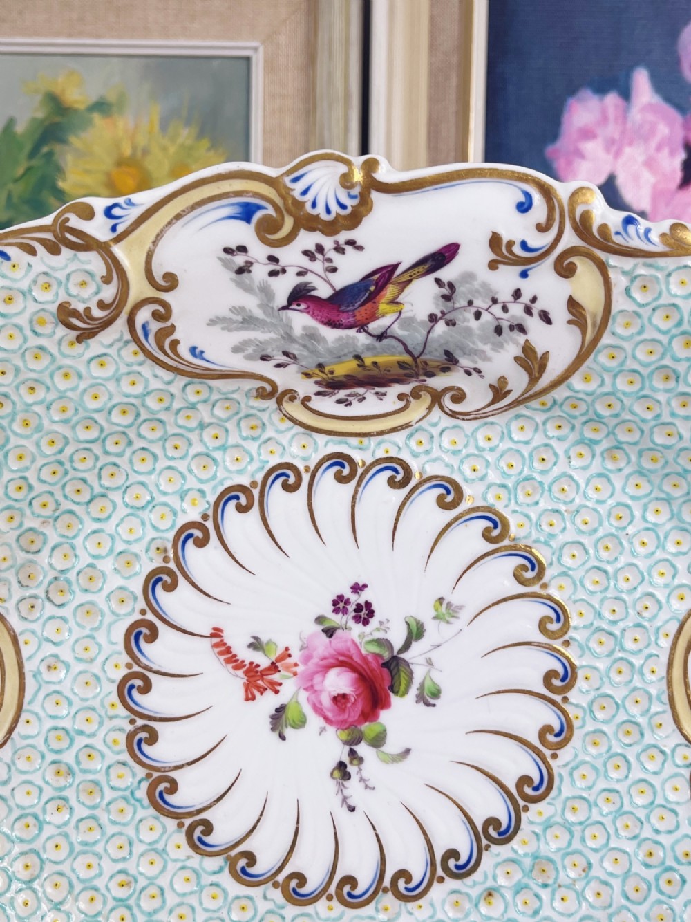 An oval antique porcelain serving dish featuring hand-painted birds in cartouches, a central pink rose, a turquoise pattern ground, and a scalloped gilded rim. View V