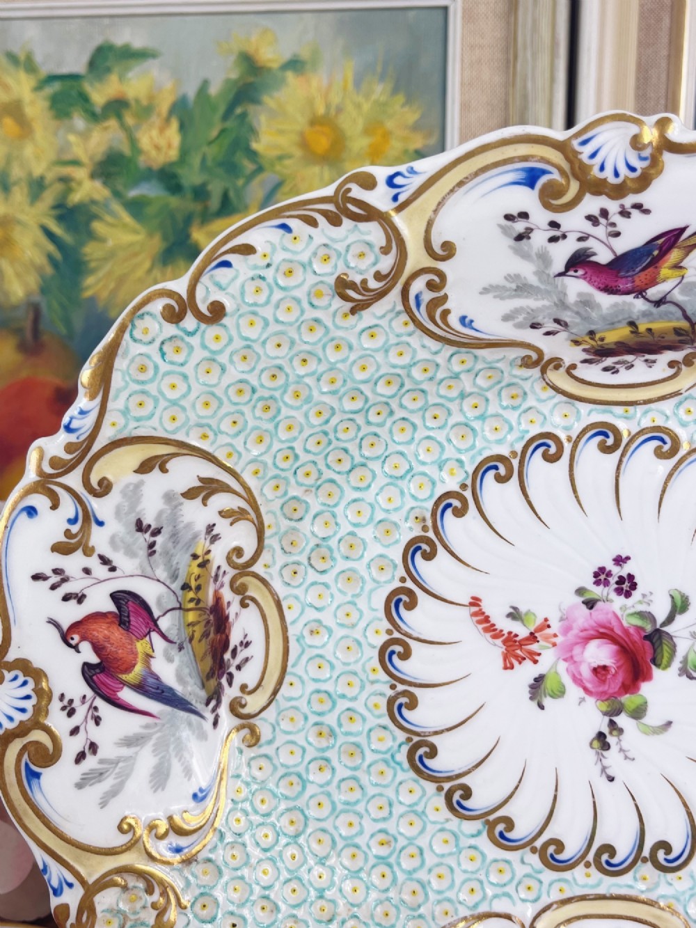An oval antique porcelain serving dish featuring hand-painted birds in cartouches, a central pink rose, a turquoise pattern ground, and a scalloped gilded rim. View VI