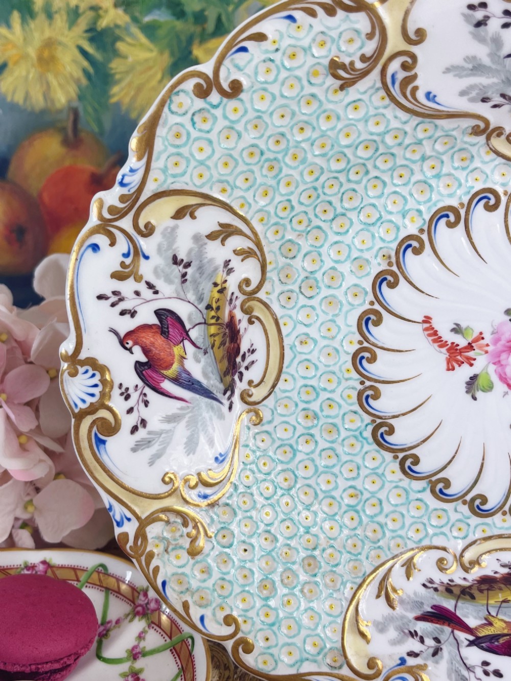 An oval antique porcelain serving dish featuring hand-painted birds in cartouches, a central pink rose, a turquoise pattern ground, and a scalloped gilded rim. View VII