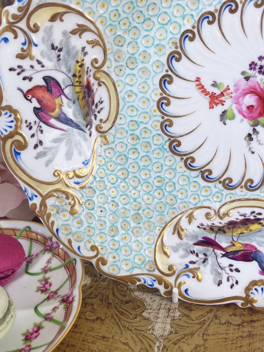 An oval antique porcelain serving dish featuring hand-painted birds in cartouches, a central pink rose, a turquoise pattern ground, and a scalloped gilded rim. View VIII