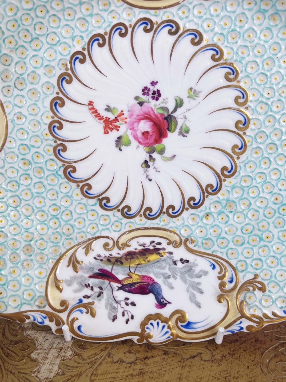 An oval antique porcelain serving dish featuring hand-painted birds in cartouches, a central pink rose, a turquoise pattern ground, and a scalloped gilded rim. View IX