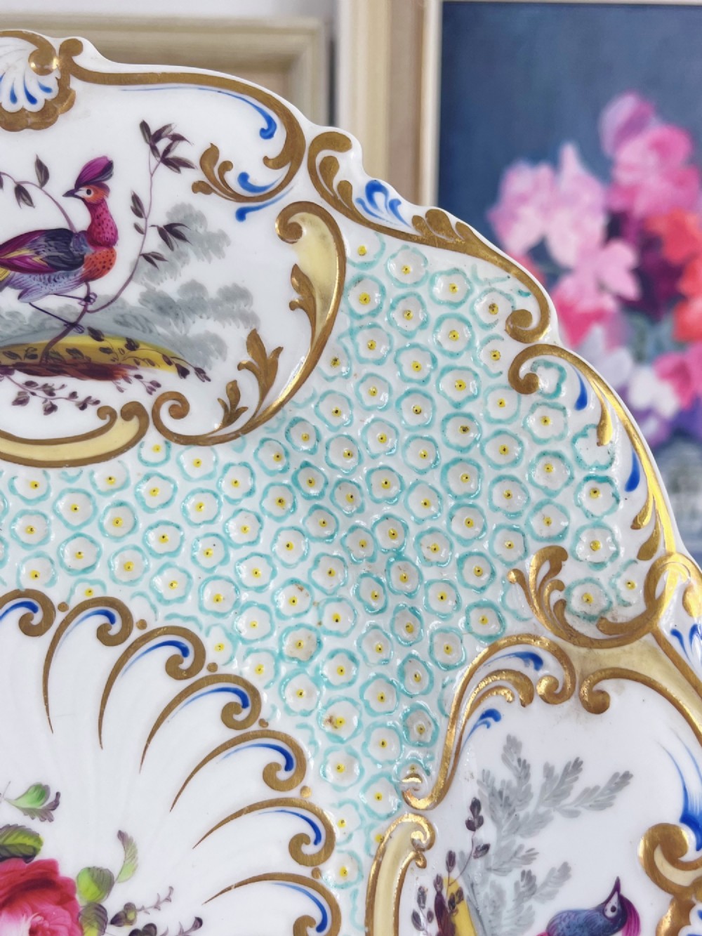 An oval antique porcelain serving dish featuring hand-painted birds in cartouches, a central pink rose, a turquoise pattern ground, and a scalloped gilded rim. View XI