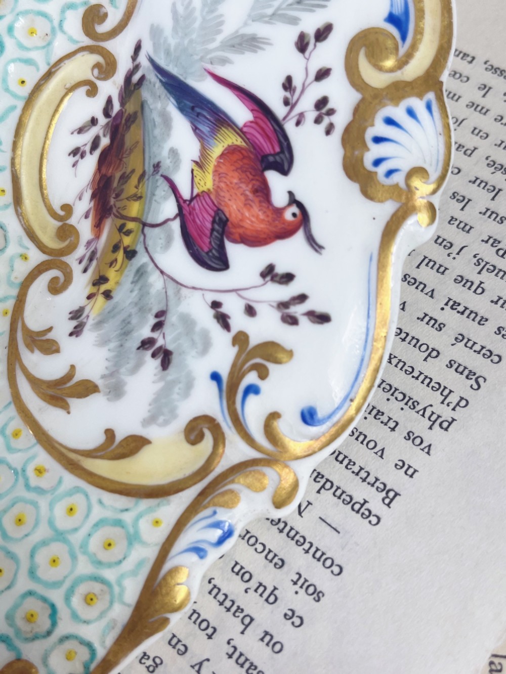 An oval antique porcelain serving dish featuring hand-painted birds in cartouches, a central pink rose, a turquoise pattern ground, and a scalloped gilded rim. View XII