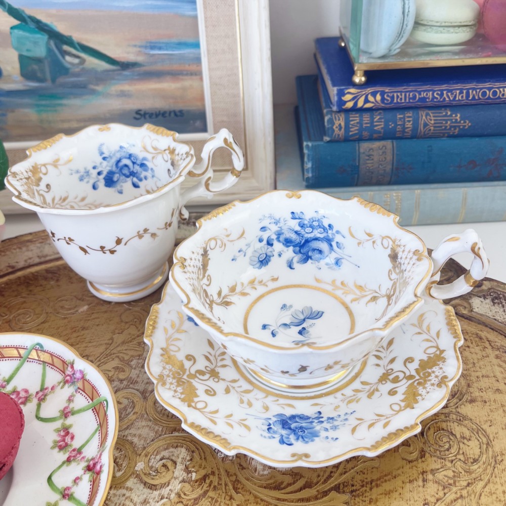 An early nineteenth-century porcelain tea and coffee cup trio featuring hand-painted blue floral motifs and gilt scroll detailing on white ground.