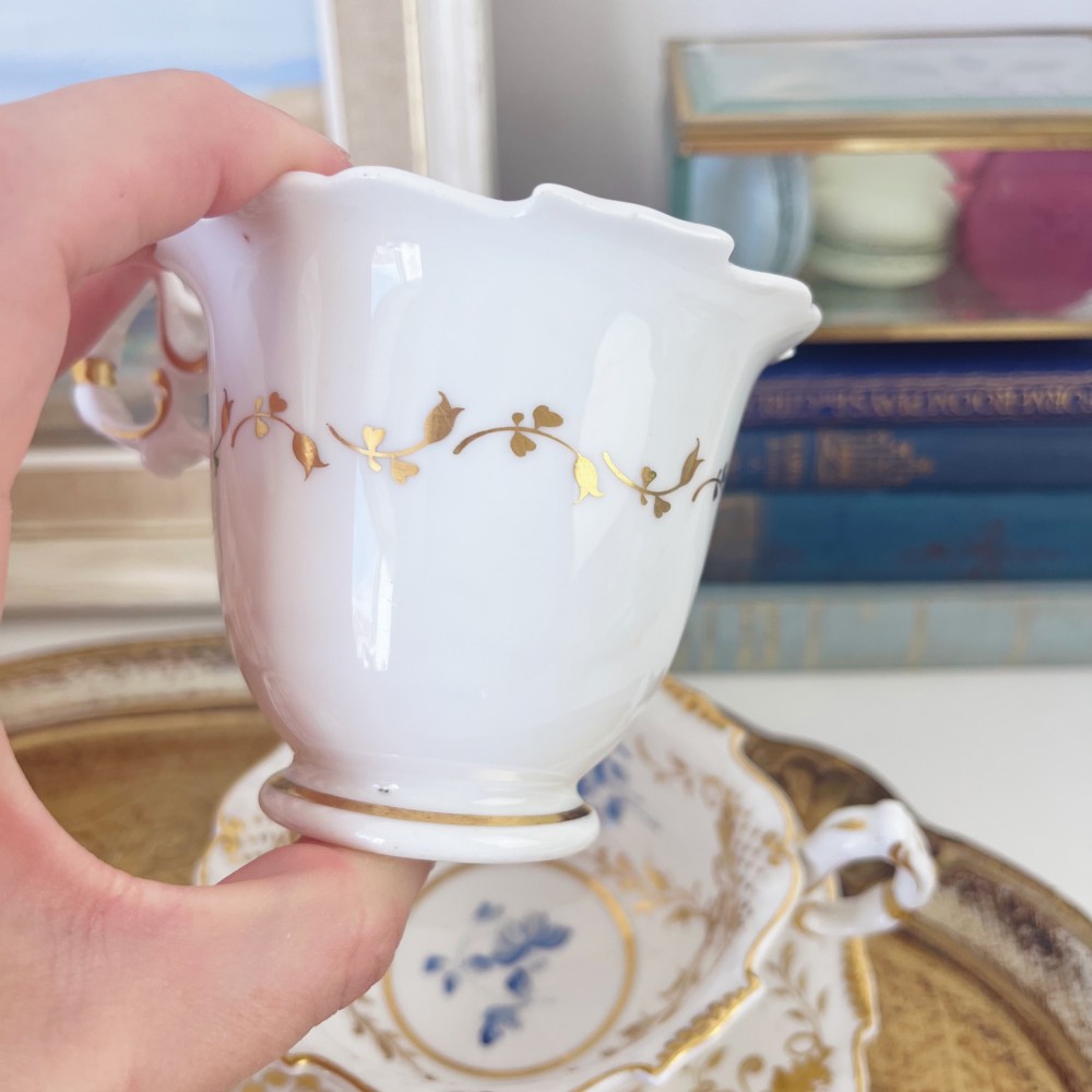 An early nineteenth-century porcelain tea and coffee cup trio featuring hand-painted blue floral motifs and gilt scroll detailing on white ground. View IV