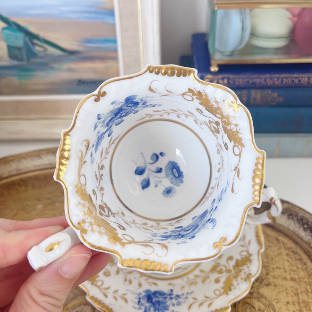 An early nineteenth-century porcelain tea and coffee cup trio featuring hand-painted blue floral motifs and gilt scroll detailing on white ground. View V