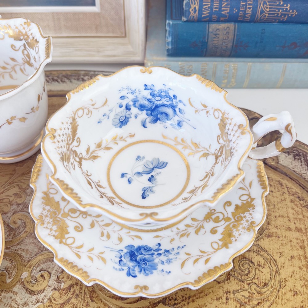 An early nineteenth-century porcelain tea and coffee cup trio featuring hand-painted blue floral motifs and gilt scroll detailing on white ground. View VI