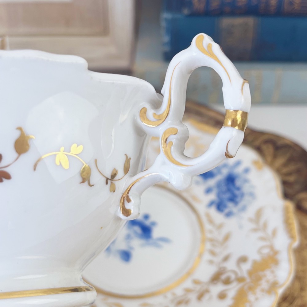An early nineteenth-century porcelain tea and coffee cup trio featuring hand-painted blue floral motifs and gilt scroll detailing on white ground. View VII