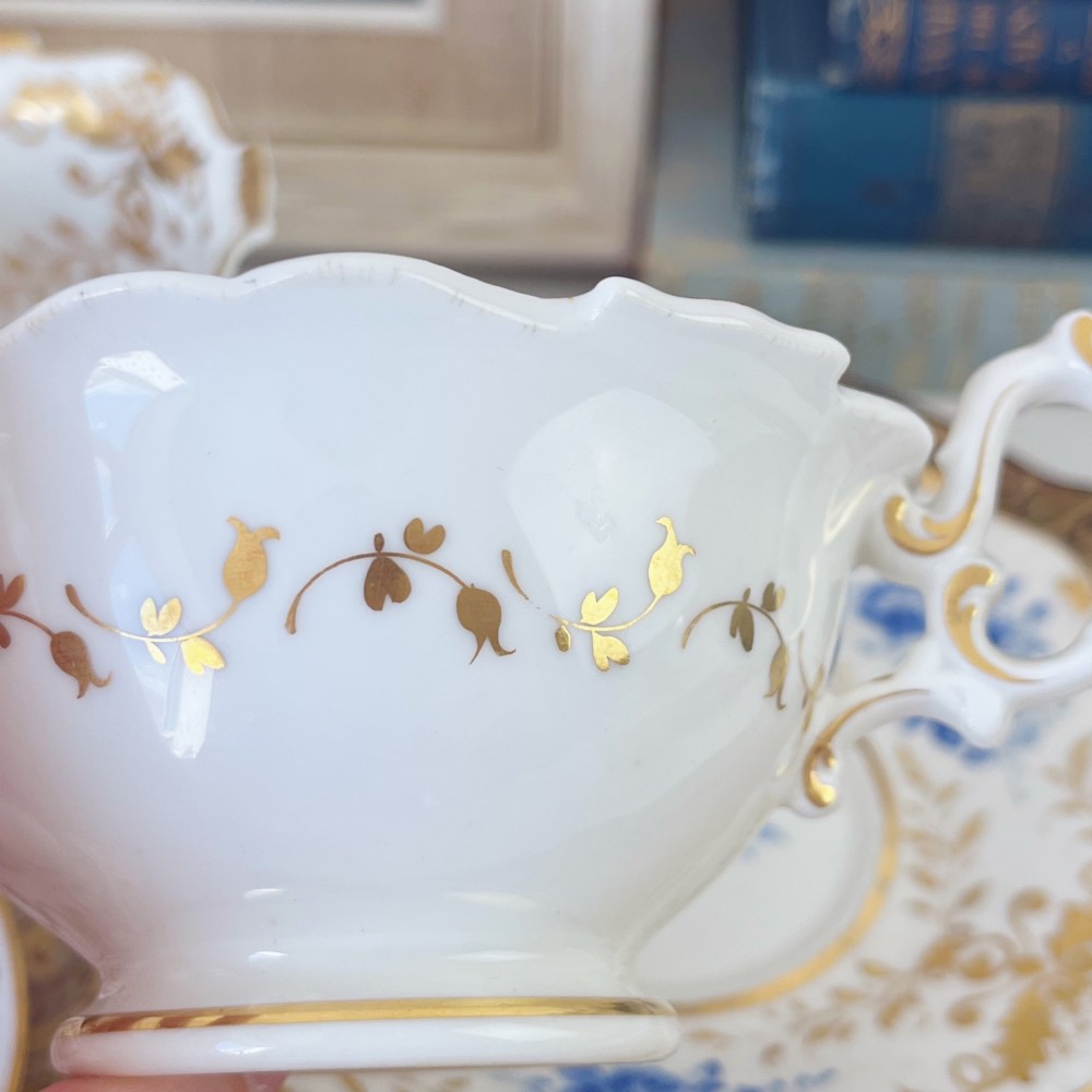 An early nineteenth-century porcelain tea and coffee cup trio featuring hand-painted blue floral motifs and gilt scroll detailing on white ground. View VIII