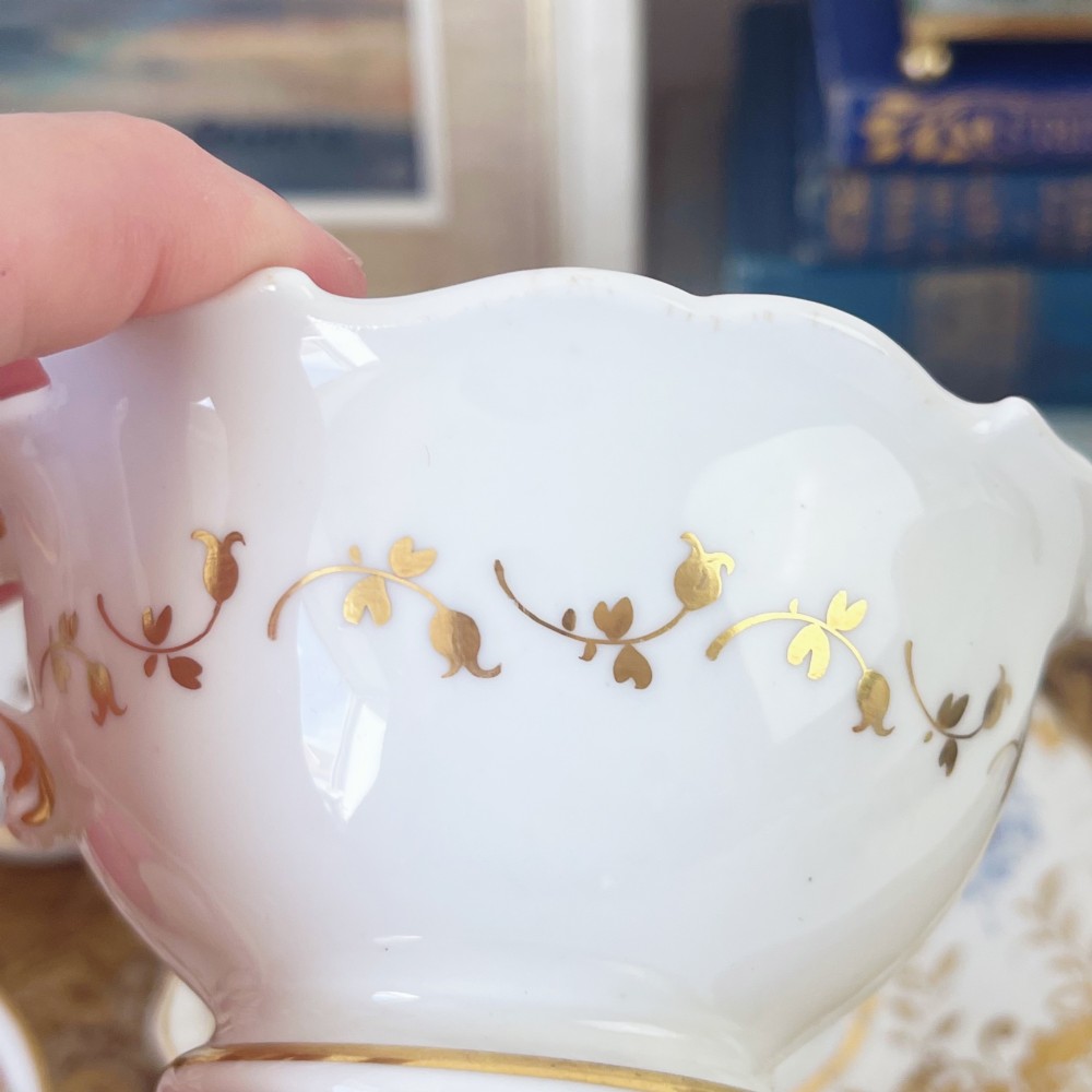 An early nineteenth-century porcelain tea and coffee cup trio featuring hand-painted blue floral motifs and gilt scroll detailing on white ground. View IX