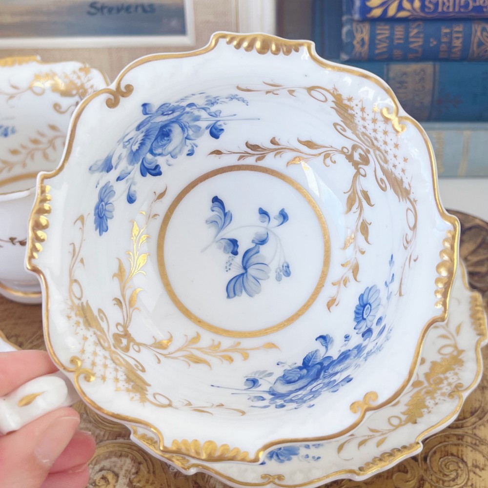An early nineteenth-century porcelain tea and coffee cup trio featuring hand-painted blue floral motifs and gilt scroll detailing on white ground. View X