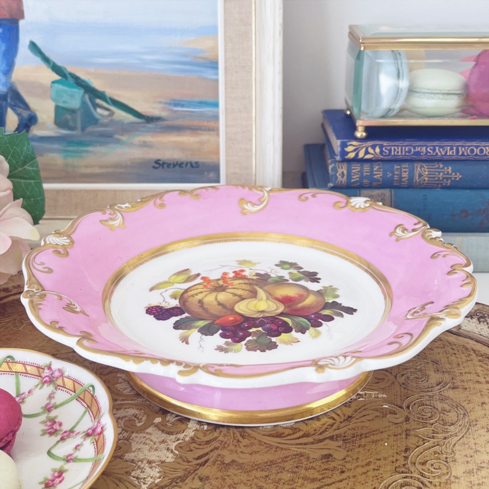 A round early nineteenth-century porcelain footed comport with a rose pink border, gilded shell edge moulding, and a hand-painted central fruit motif.