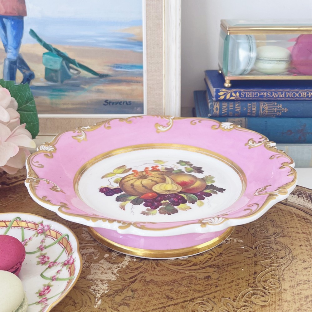 A round early nineteenth-century porcelain footed comport with a rose pink border, gilded shell edge moulding, and a hand-painted central fruit motif. View II