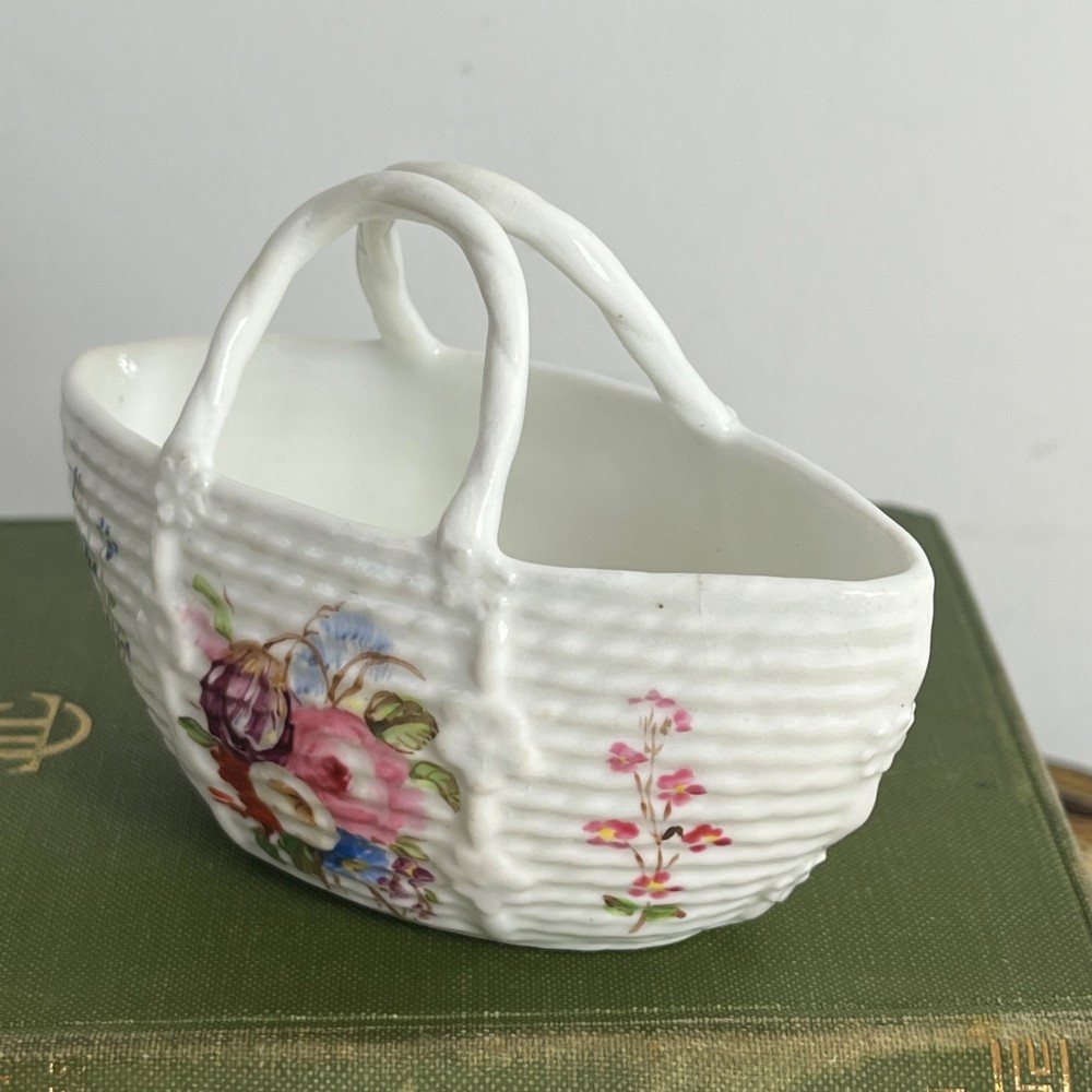 A miniature white porcelain basket featuring a raised basketweave texture, an arched handle, and hand-painted colourful floral motifs on the exterior. View II