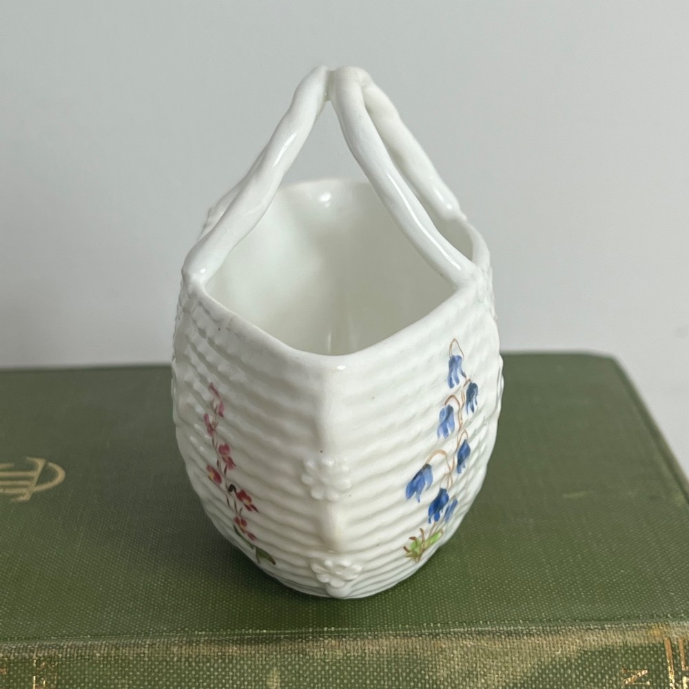 A miniature white porcelain basket featuring a raised basketweave texture, an arched handle, and hand-painted colourful floral motifs on the exterior. View III