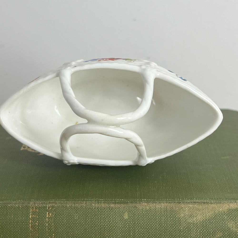 A miniature white porcelain basket featuring a raised basketweave texture, an arched handle, and hand-painted colourful floral motifs on the exterior. View VII