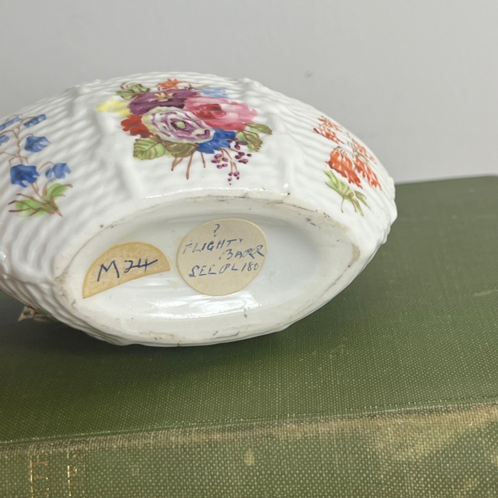A miniature white porcelain basket featuring a raised basketweave texture, an arched handle, and hand-painted colourful floral motifs on the exterior. View VIII