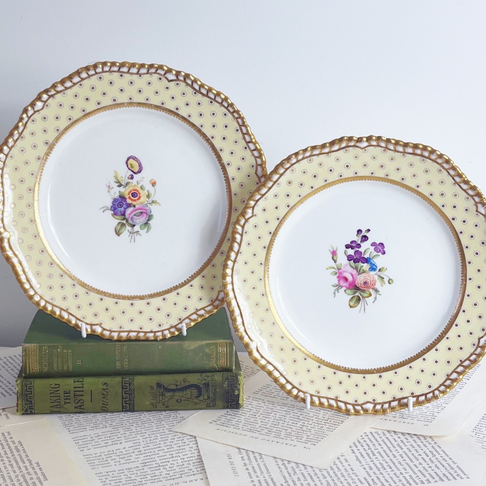 A pair of Regency period Spode Felspar porcelain dessert plates featuring pale yellow patterned rims with gilded scalloped edges and central hand-painted floral sprays.