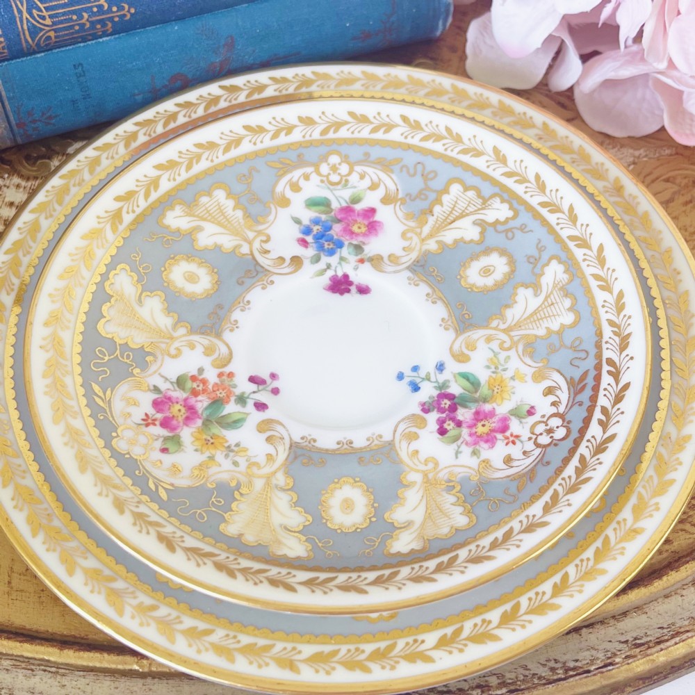 An antique Cauldon bone china teacup trio featuring powder blue borders, intricate gilt scrollwork, and hand-painted floral vignettes on white porcelain. View VIII