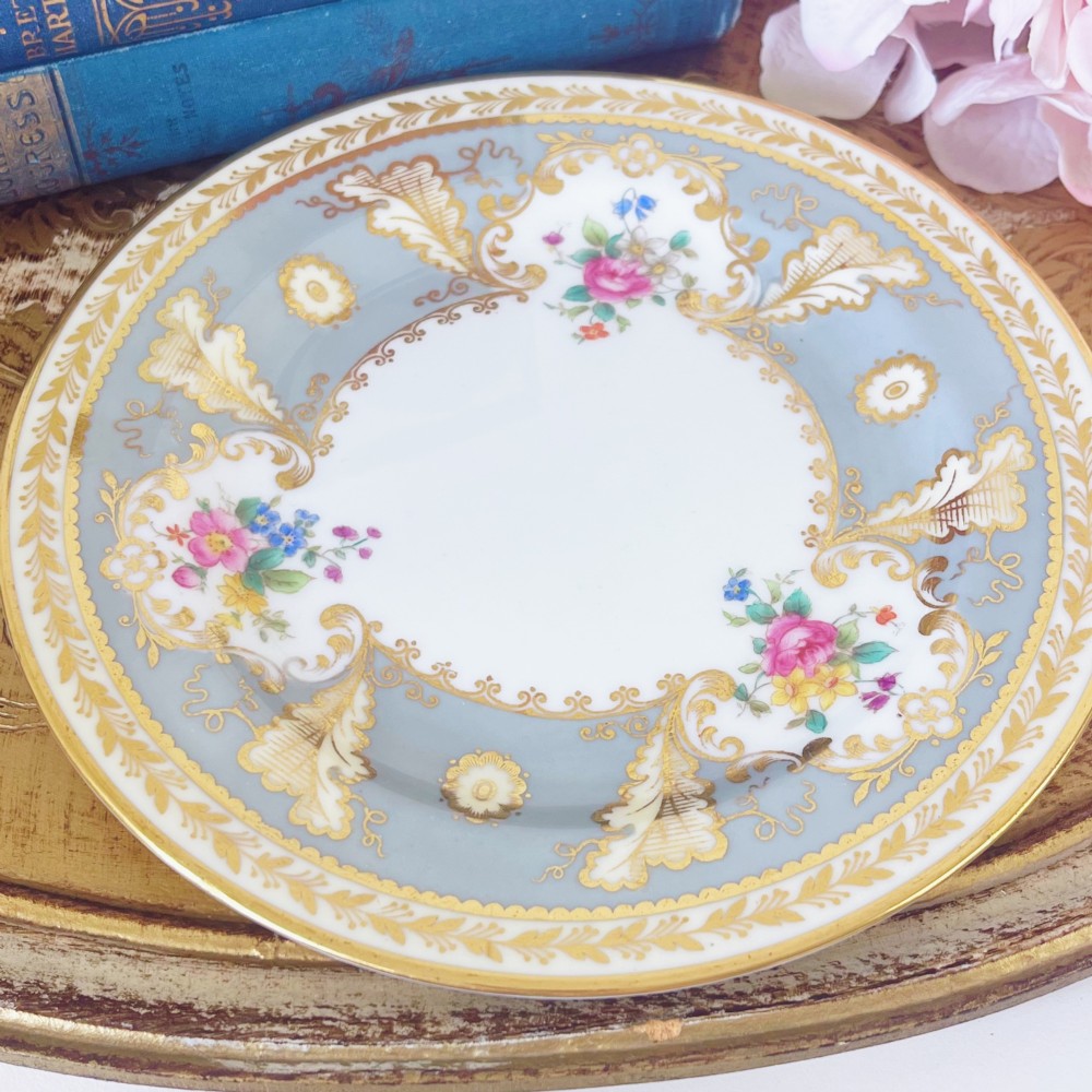 An antique Cauldon bone china teacup trio featuring powder blue borders, intricate gilt scrollwork, and hand-painted floral vignettes on white porcelain. View IX