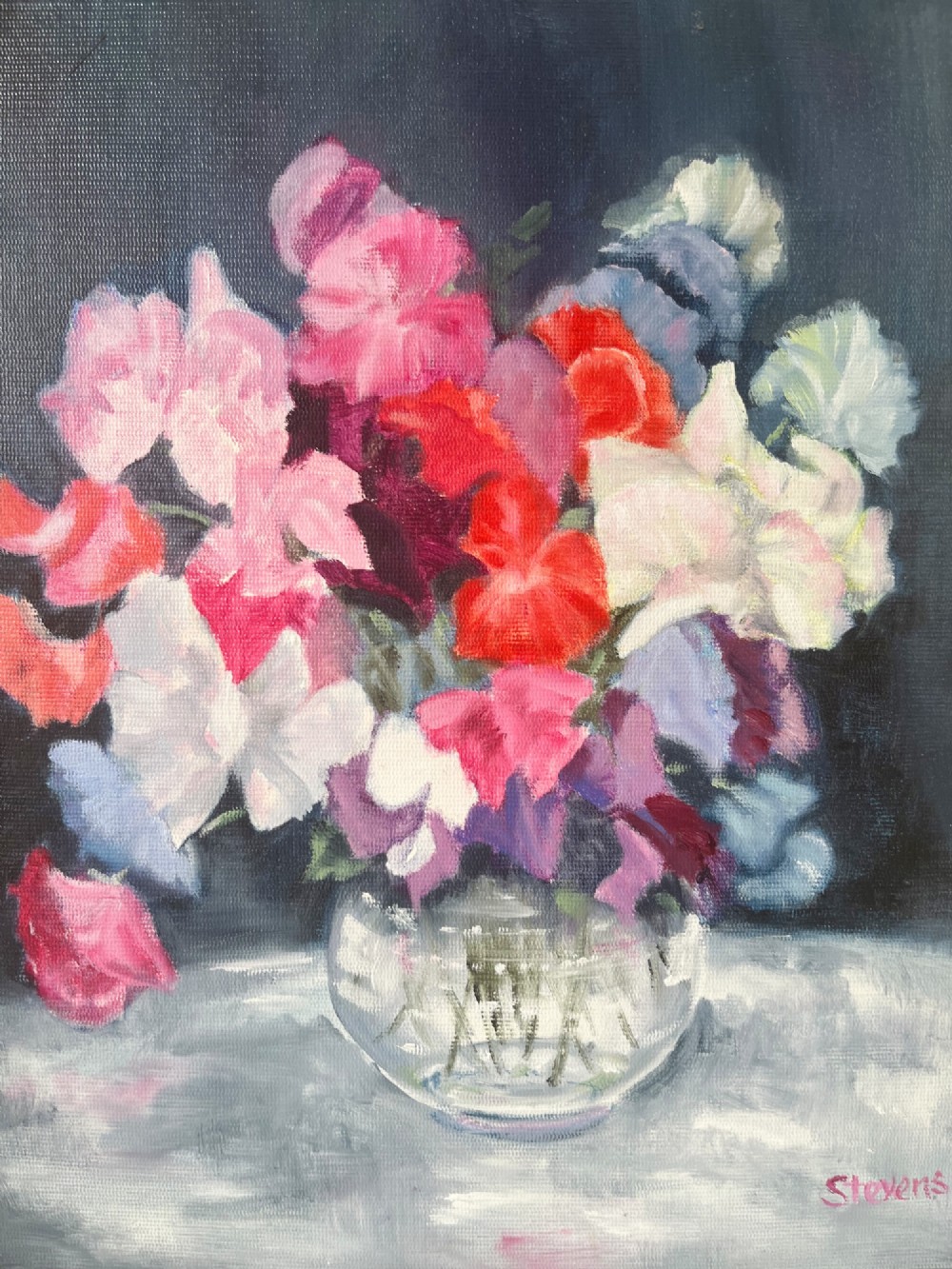 A framed oil painting depicting a colourful bouquet of pink, red, and purple sweet peas in a clear glass vase set against a dark blue background. View II