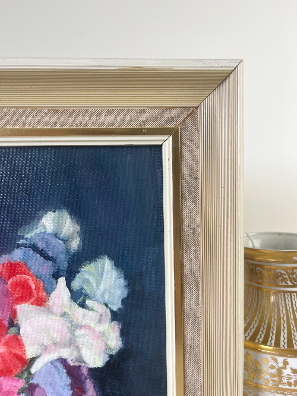 A framed oil painting depicting a colourful bouquet of pink, red, and purple sweet peas in a clear glass vase set against a dark blue background. View III