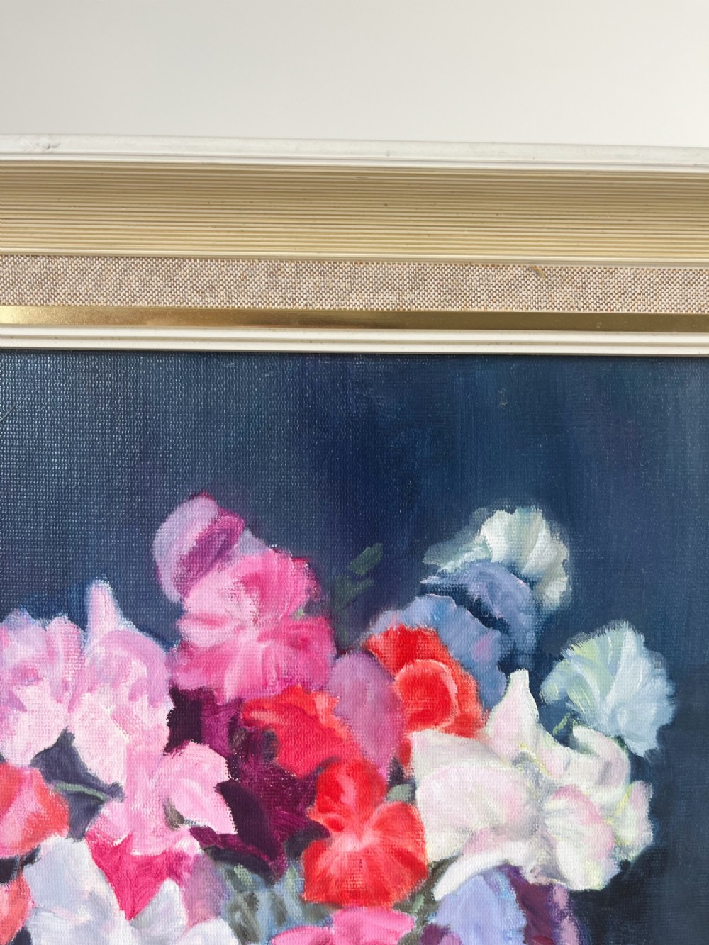 A framed oil painting depicting a colourful bouquet of pink, red, and purple sweet peas in a clear glass vase set against a dark blue background. View IV