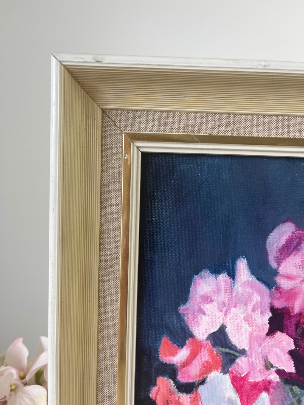 A framed oil painting depicting a colourful bouquet of pink, red, and purple sweet peas in a clear glass vase set against a dark blue background. View V