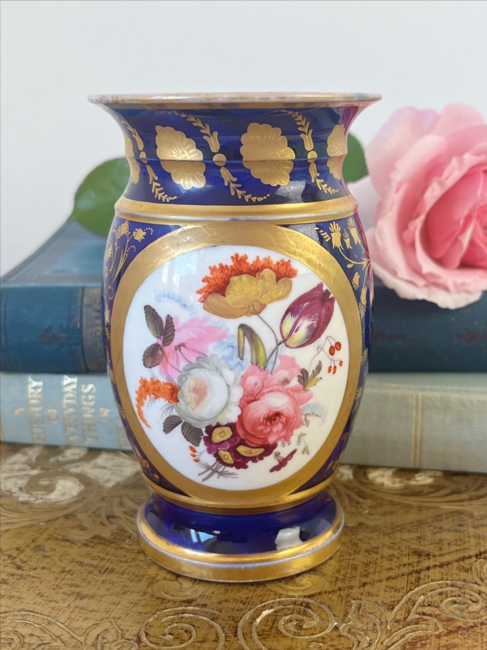 A small cylindrical Regency Coalport porcelain spill vase featuring a cobalt blue ground with gold leaf accents and a central oval medallion hand-painted with flowers.