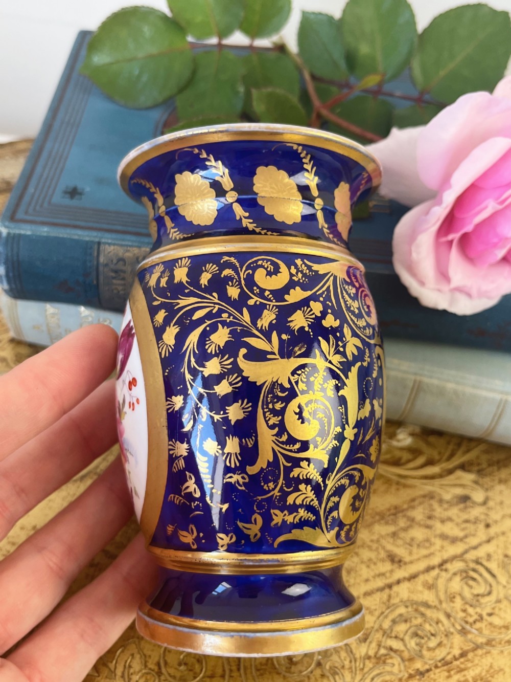 A small cylindrical Regency Coalport porcelain spill vase featuring a cobalt blue ground with gold leaf accents and a central oval medallion hand-painted with flowers. View V