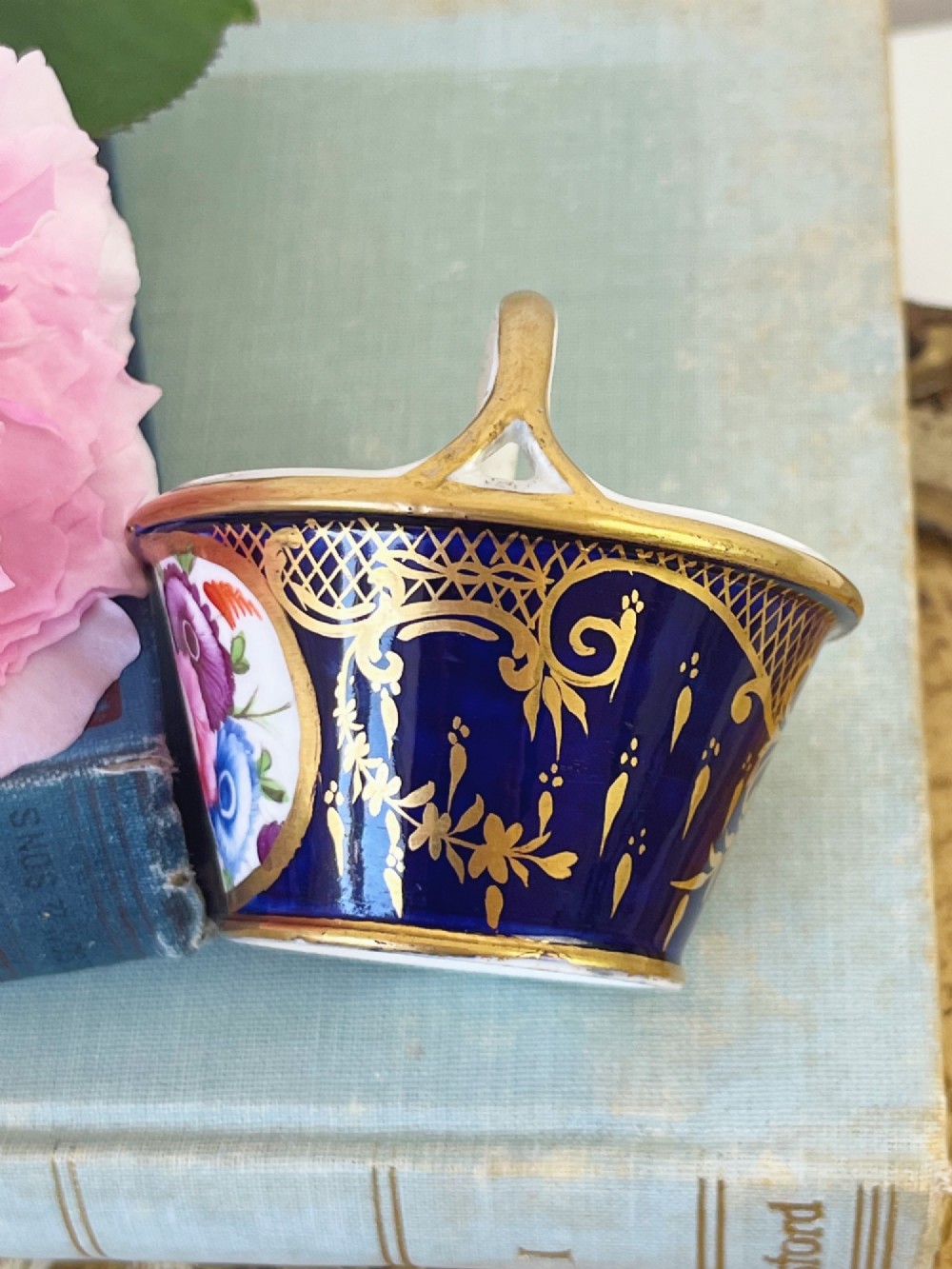 A miniature Regency Coalport porcelain basket featuring an overhead gilt handle, cobalt blue exterior casing with a hand-painted floral reserve, and a plain white interior. View III