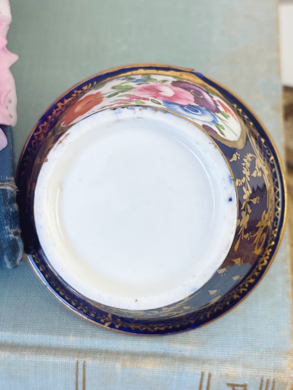 A miniature Regency Coalport porcelain basket featuring an overhead gilt handle, cobalt blue exterior casing with a hand-painted floral reserve, and a plain white interior. View VI
