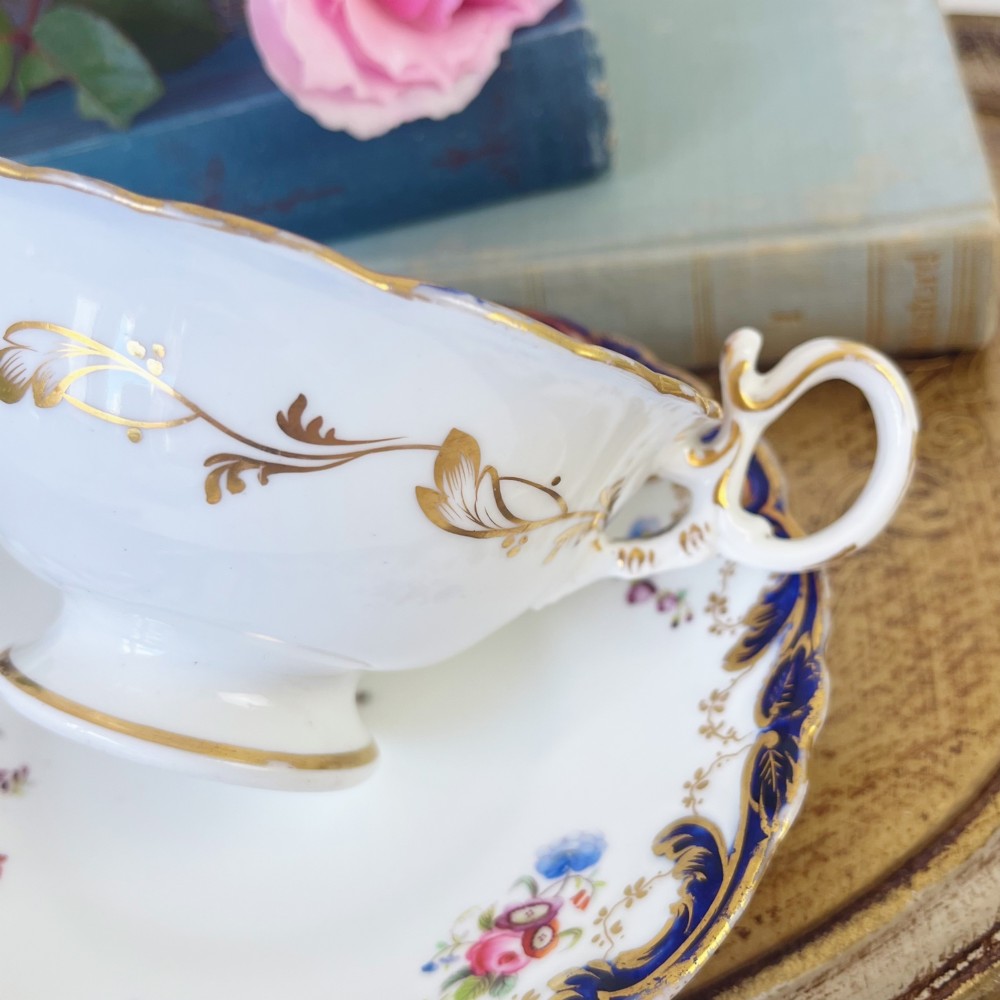 An antique bone china teacup and saucer set featuring cobalt blue scroll borders, gilded ornamentation, and hand-painted floral sprays on a white ground. View III