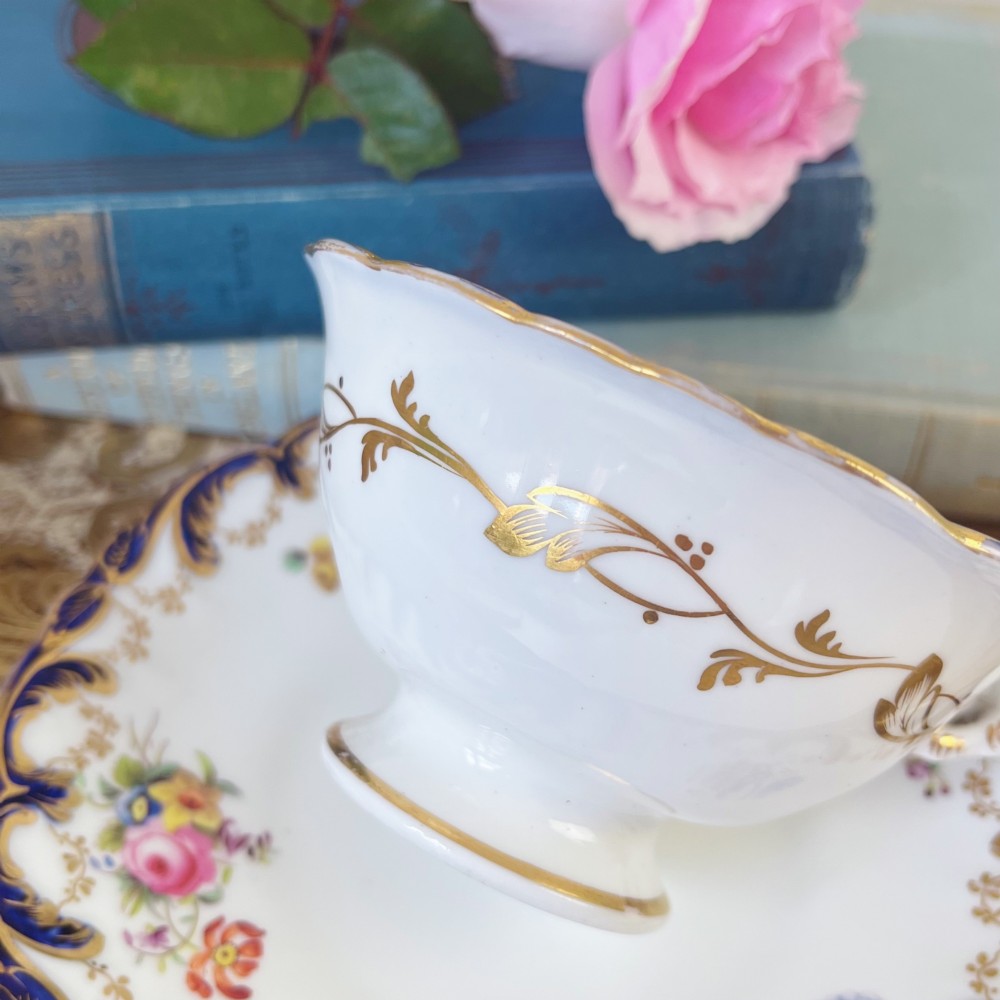An antique bone china teacup and saucer set featuring cobalt blue scroll borders, gilded ornamentation, and hand-painted floral sprays on a white ground. View IV
