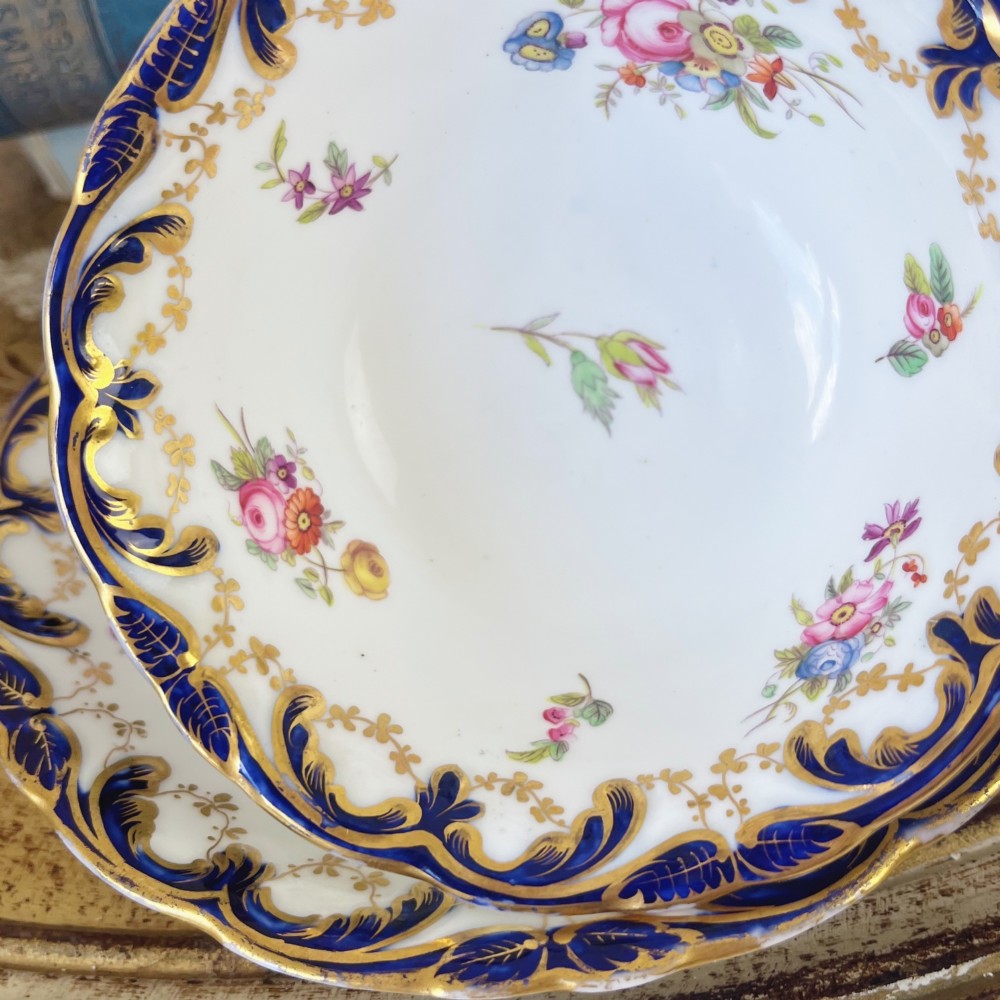 An antique bone china teacup and saucer set featuring cobalt blue scroll borders, gilded ornamentation, and hand-painted floral sprays on a white ground. View V