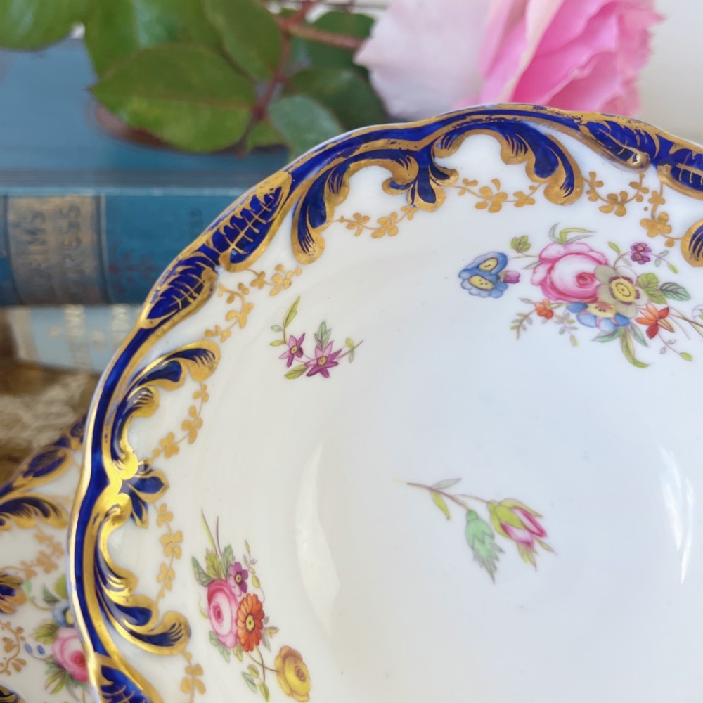 An antique bone china teacup and saucer set featuring cobalt blue scroll borders, gilded ornamentation, and hand-painted floral sprays on a white ground. View VI