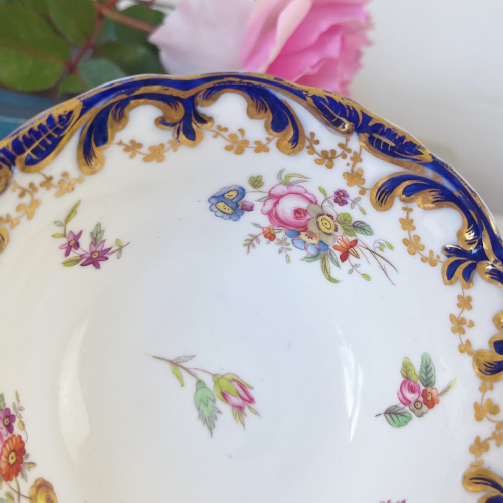 An antique bone china teacup and saucer set featuring cobalt blue scroll borders, gilded ornamentation, and hand-painted floral sprays on a white ground. View VII