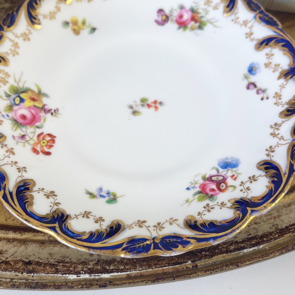 An antique bone china teacup and saucer set featuring cobalt blue scroll borders, gilded ornamentation, and hand-painted floral sprays on a white ground. View IX