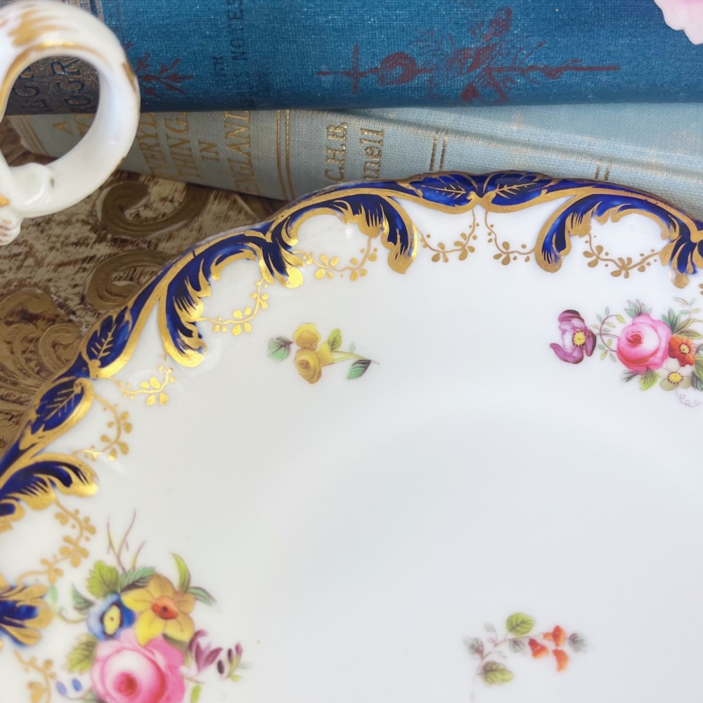 An antique bone china teacup and saucer set featuring cobalt blue scroll borders, gilded ornamentation, and hand-painted floral sprays on a white ground. View XI