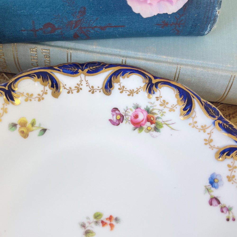 An antique bone china teacup and saucer set featuring cobalt blue scroll borders, gilded ornamentation, and hand-painted floral sprays on a white ground. View XII