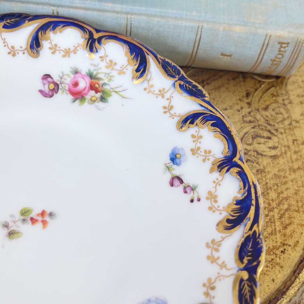 An antique bone china teacup and saucer set featuring cobalt blue scroll borders, gilded ornamentation, and hand-painted floral sprays on a white ground. View XIII