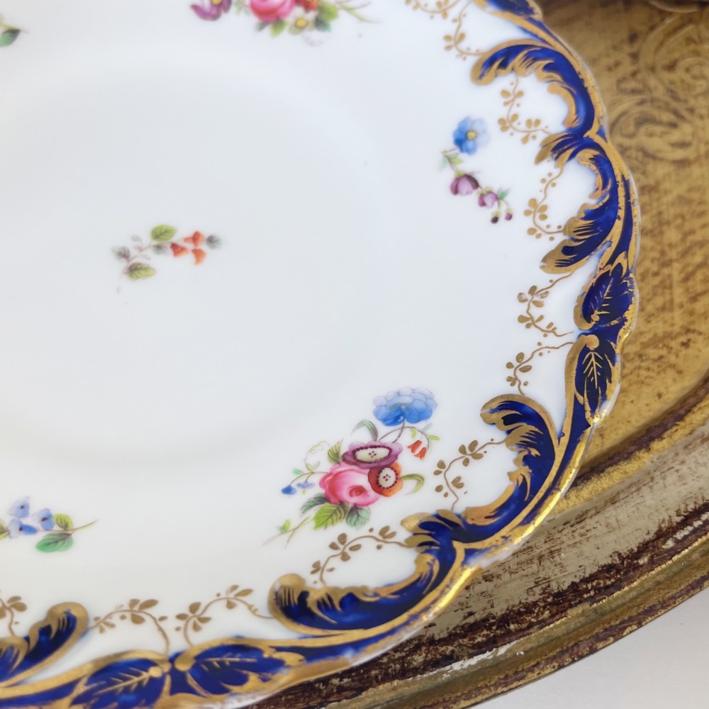 An antique bone china teacup and saucer set featuring cobalt blue scroll borders, gilded ornamentation, and hand-painted floral sprays on a white ground. View XIV