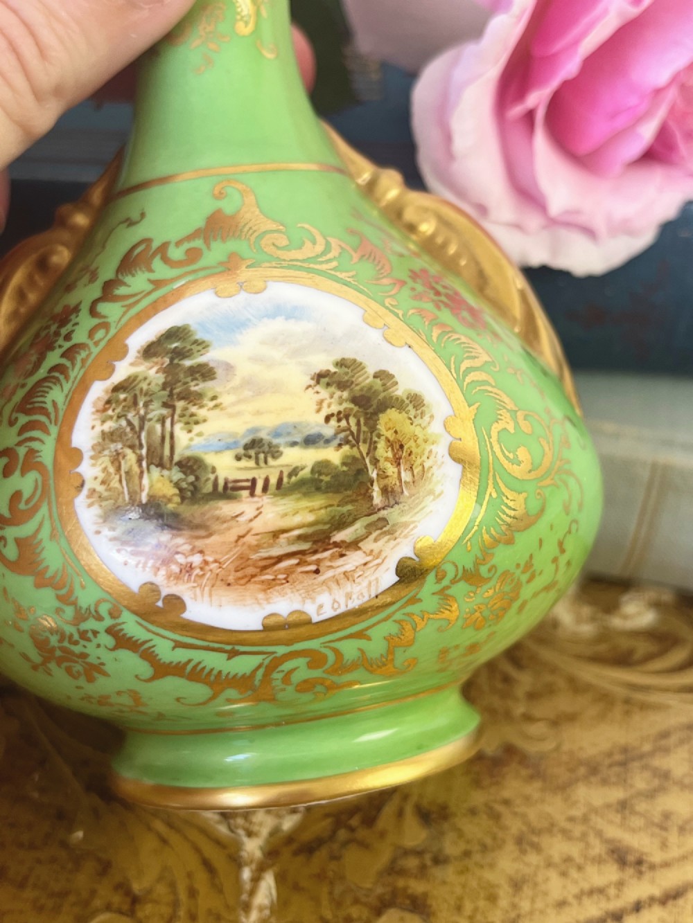 An apple green ceramic miniature vase featuring gilded handles, gold scrollwork accents, and a hand-painted landscape scene inside a central circular medallion. View II