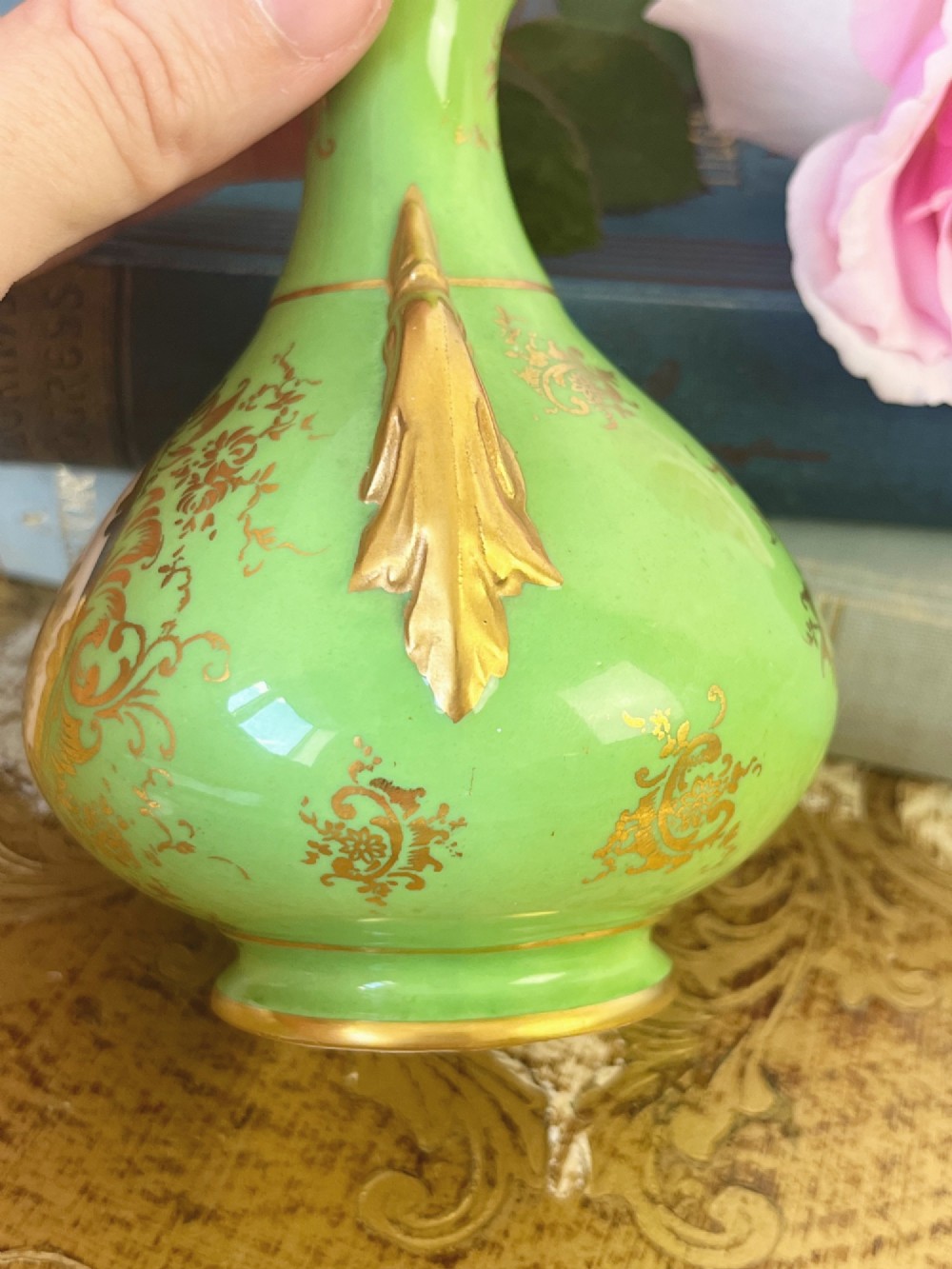 An apple green ceramic miniature vase featuring gilded handles, gold scrollwork accents, and a hand-painted landscape scene inside a central circular medallion. View III