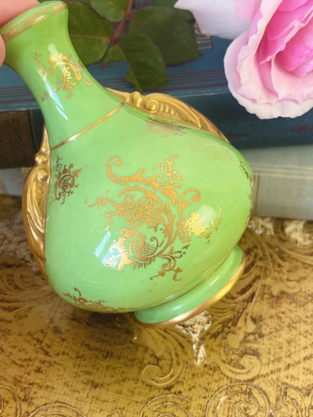 An apple green ceramic miniature vase featuring gilded handles, gold scrollwork accents, and a hand-painted landscape scene inside a central circular medallion. View IV