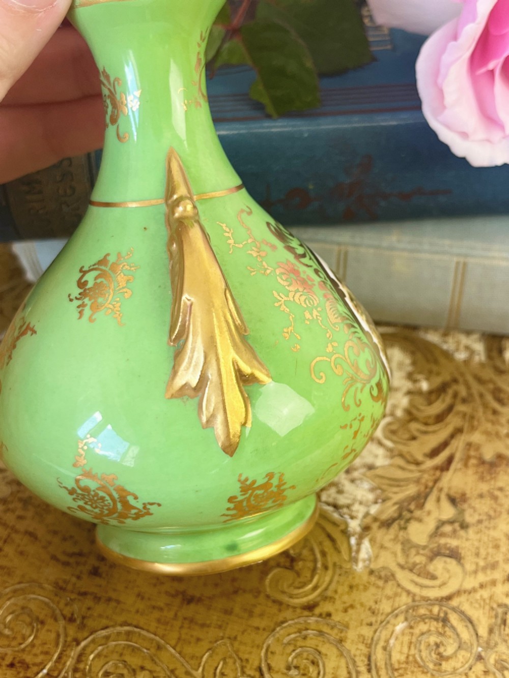 An apple green ceramic miniature vase featuring gilded handles, gold scrollwork accents, and a hand-painted landscape scene inside a central circular medallion. View V