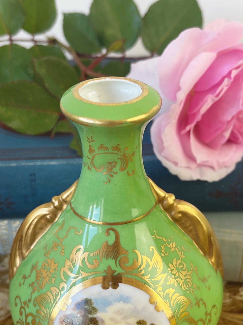 An apple green ceramic miniature vase featuring gilded handles, gold scrollwork accents, and a hand-painted landscape scene inside a central circular medallion. View VI