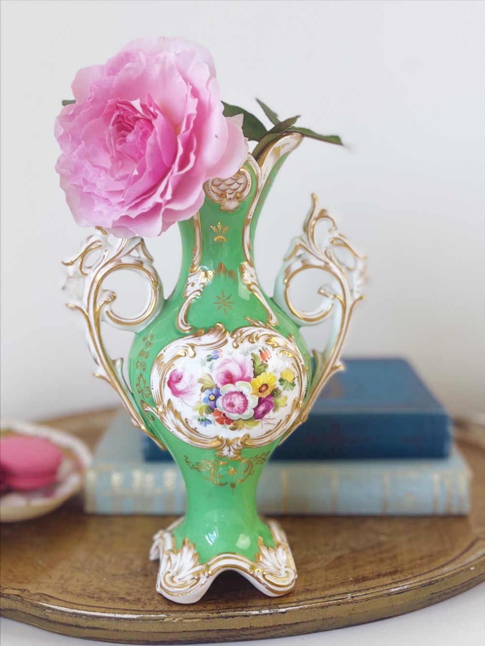 An apple green Rococo Revival porcelain vase featuring ornate gilded scroll handles, a quad-lobed pedestal base, and a central handpainted floral medallion on a white background.